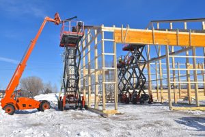Hoists lifts, and scissor lifts are being used in the construction of a new industrial warehouse in icy conditions.