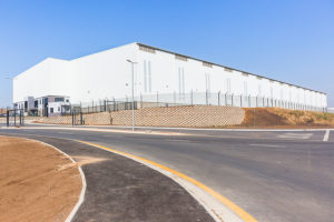 Scale your business by leasing construction equipment; New warehouse factory building structure for business constructed covering off white panels and new roads outdoors blue skies.