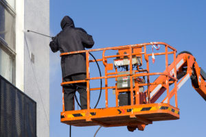 Worker In Black Uniform Wash A White Building Wall on Aerial Lift Platform; pressure washing business